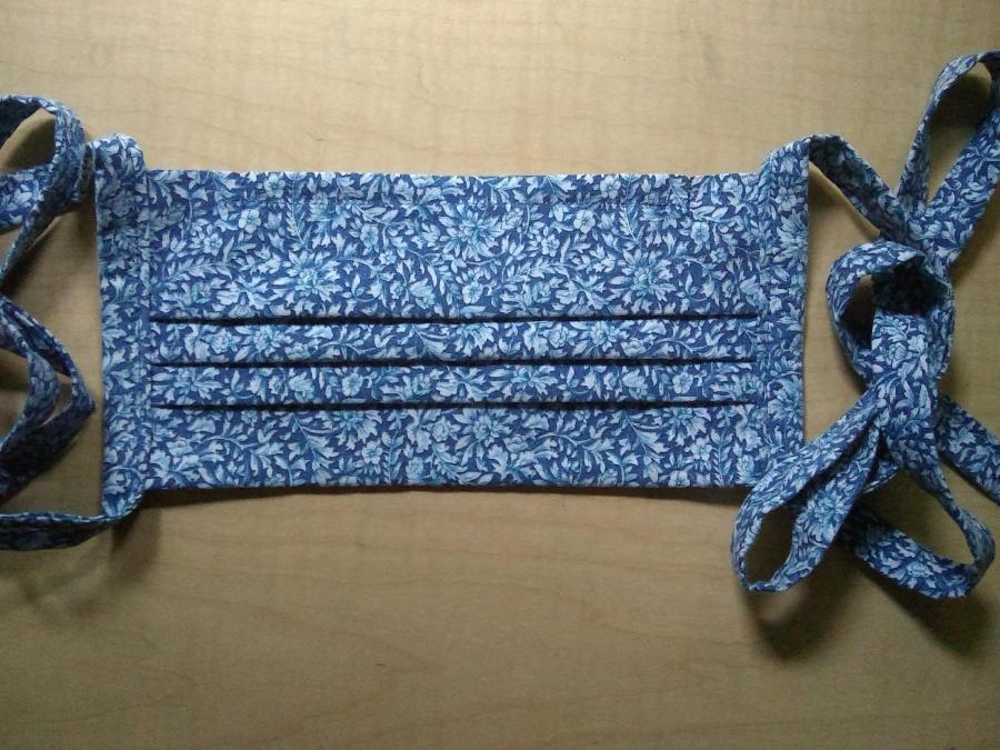 Pleated mask in blue flowered print with cloth ties, lying on wooden background