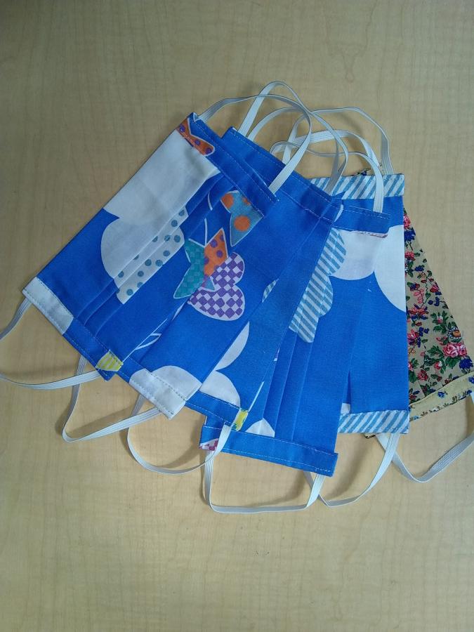 several pleated cloth face masks with elastic loops, most in blue fabric