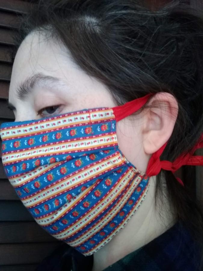 sideview of woman wearing pleated face mask with cloth ties that loop around the ear and then tie at the back of the head