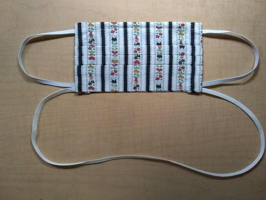 pleated facemask with elastic earloops and neck cord, white flowered print, lying on wooden background