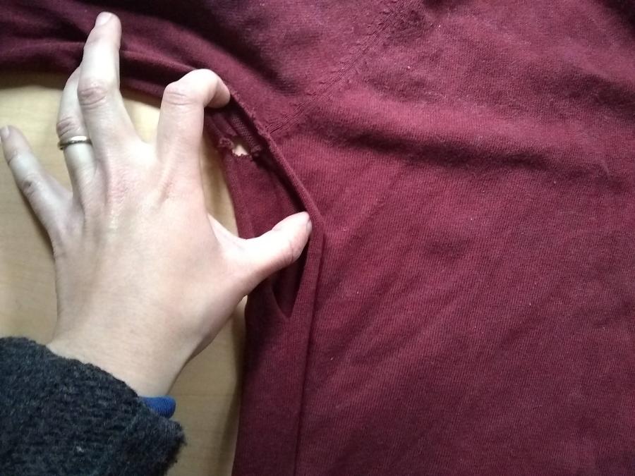 closeup of hand showing length of large hole in armpit seam with small hole also showing