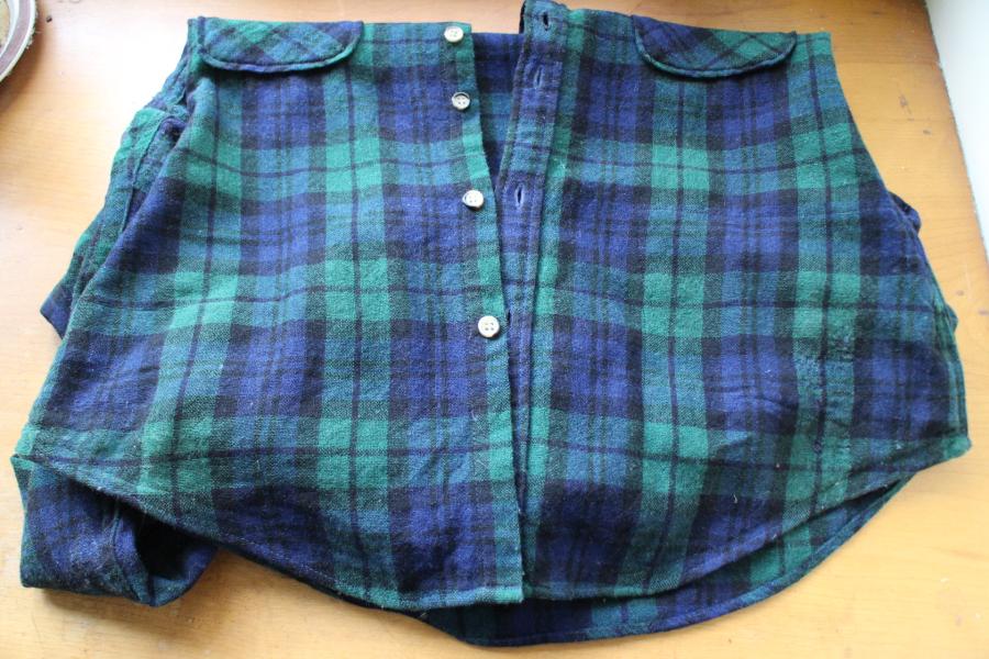 folded black watch plaid shirt on wooden background showing bottom front with invisible mending