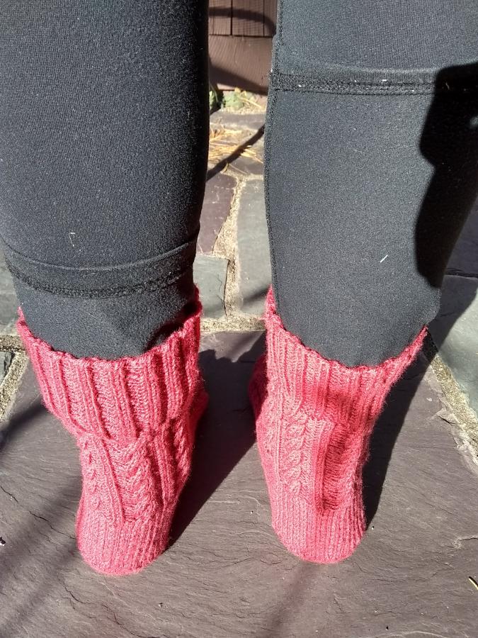 back view of feet wearing pinkish red cabled socks outdoors on patio