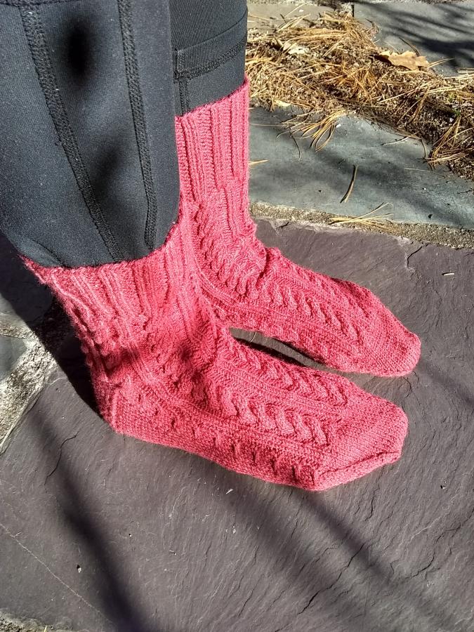 side view of feet wearing pinkish red cabled socks outdoors on patio