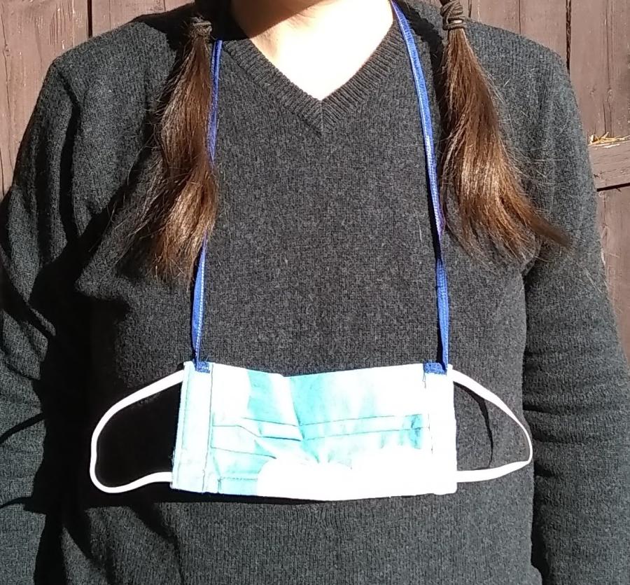 woman's torso with pleated face mask with elastic ear loops hanging around neck by neck cord
