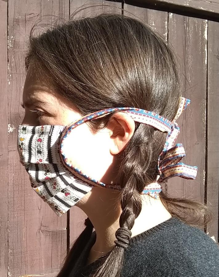 side view of woman wearing pleated face mask with contrasting cloth ties tied around back of head