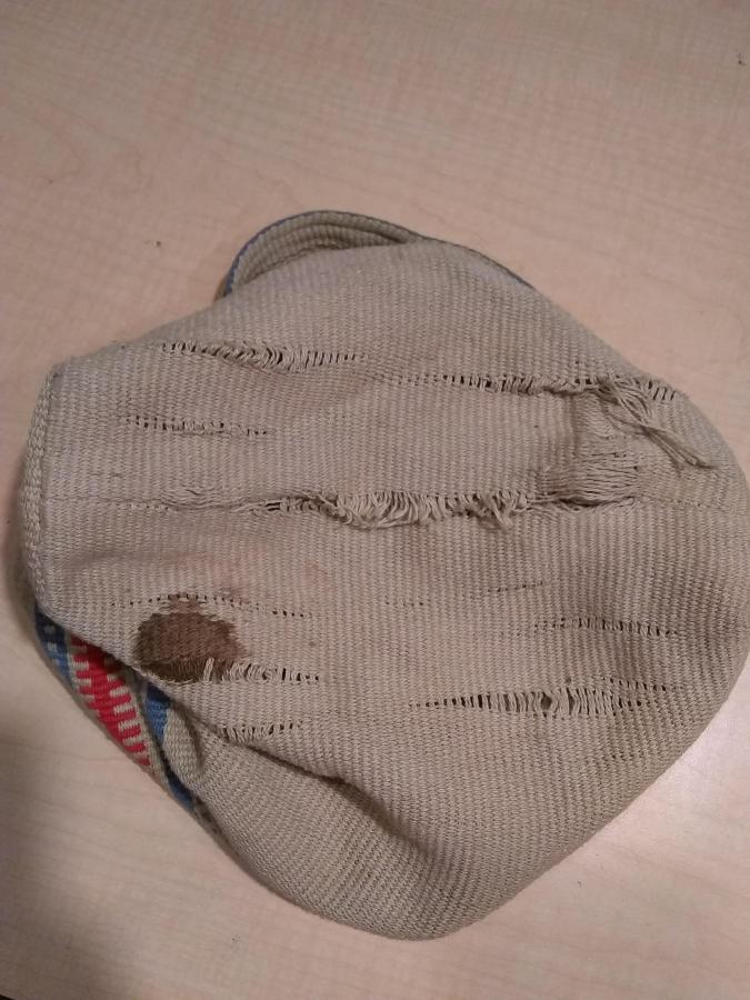 view of the bottom of beige hand woven bag showing stain and worn fabric