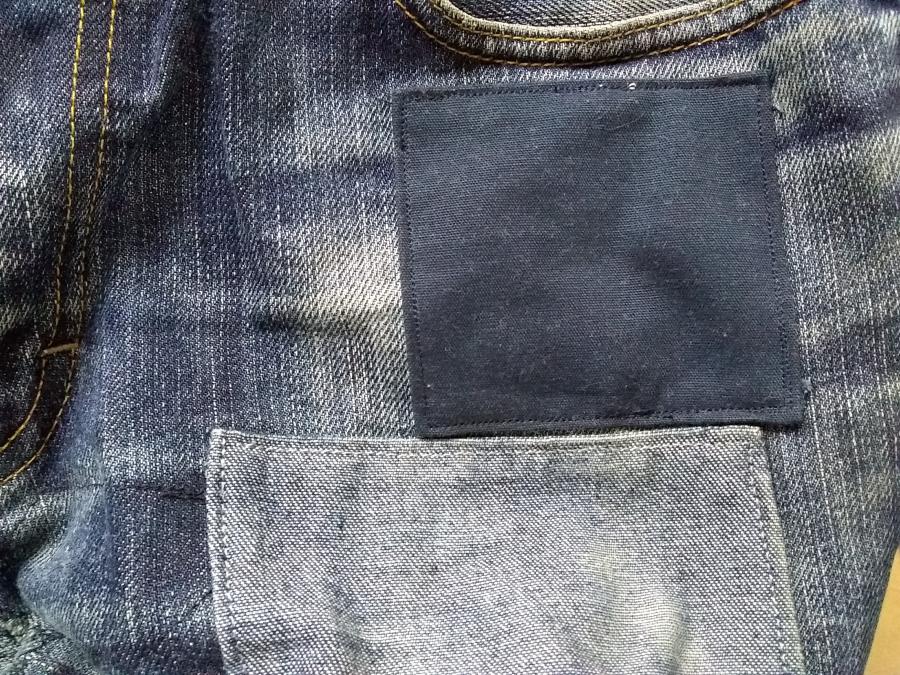 closeup of one side of jeans front under pocket, showing new (navy blue) and old (pale denim) patches