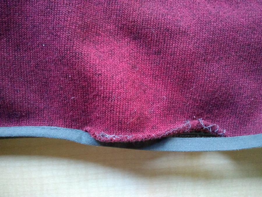 Closeup of bottom of red fleece sweater showing that sewing attaching binding to sweater has come undone