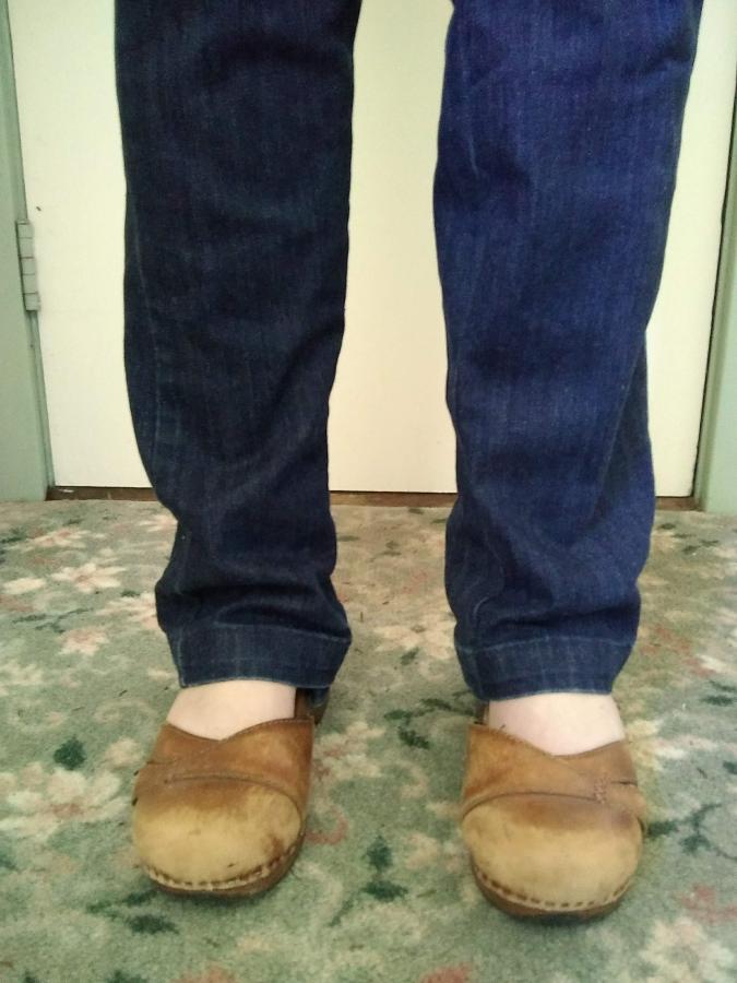 front view of woman's ankles and feet in too-long dark jeans and brown leather shoes