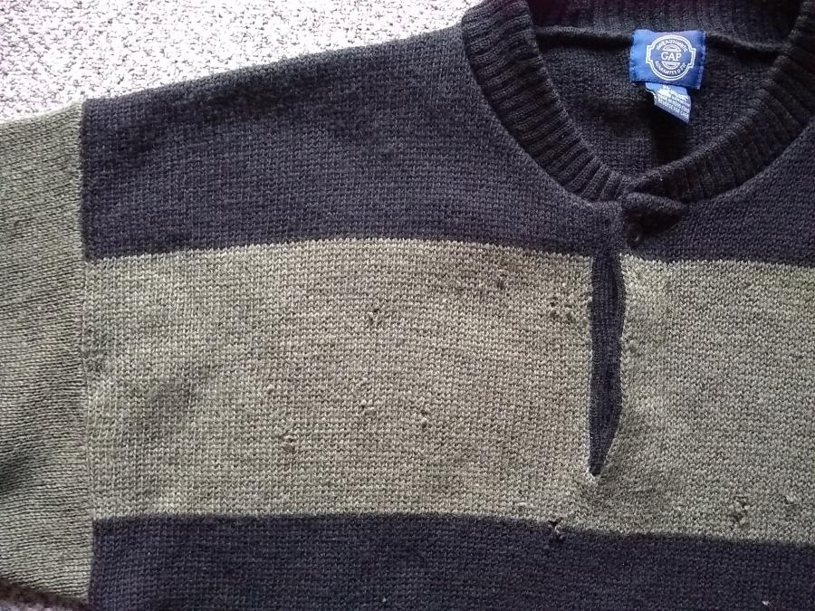 closeup of holes on the front chest, right side, of olive and black sweater