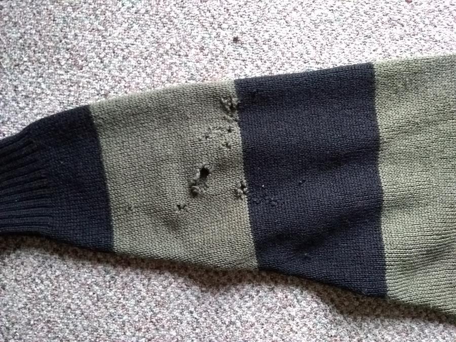 closeup of holes on sleeve of olive and black sweater