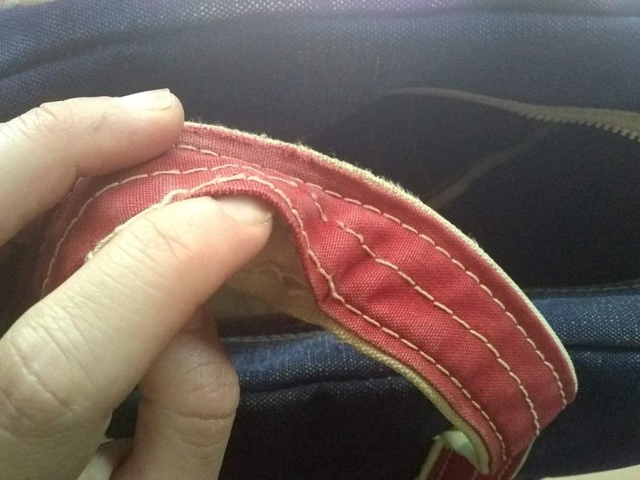 closeup of falling apart handle stitching on tote bag, shown by finger of hand being able to get inside two layers of handle