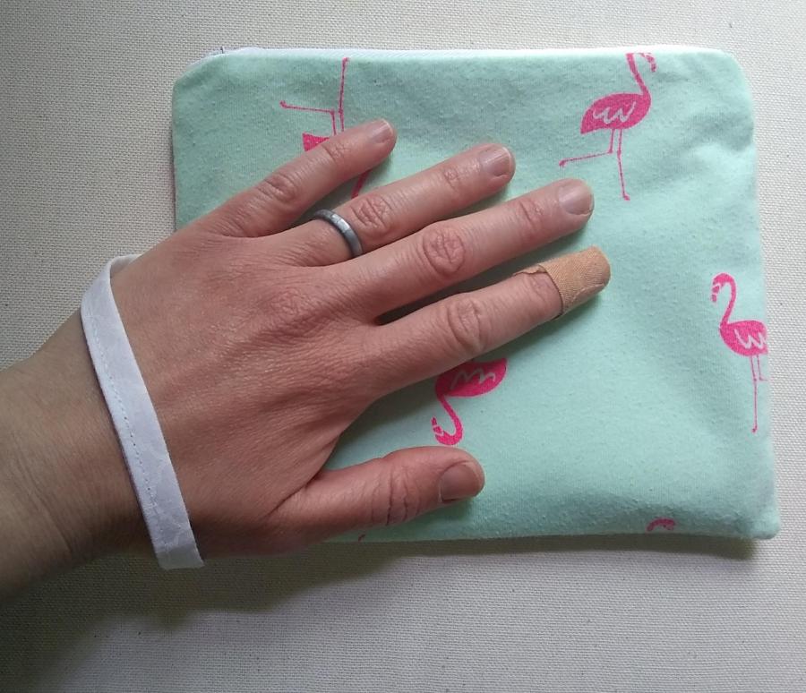 wristlet (little purse with wrist strap), pale green with pink flamingos, held in hand with white wrist loop