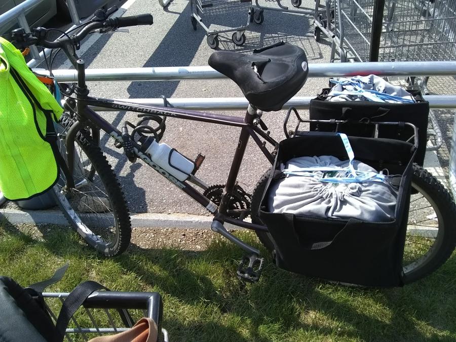 Bike leaning against grocery cart enclosure, with pannier liner bags full, drawstring of liner bags tied and secured in panniers