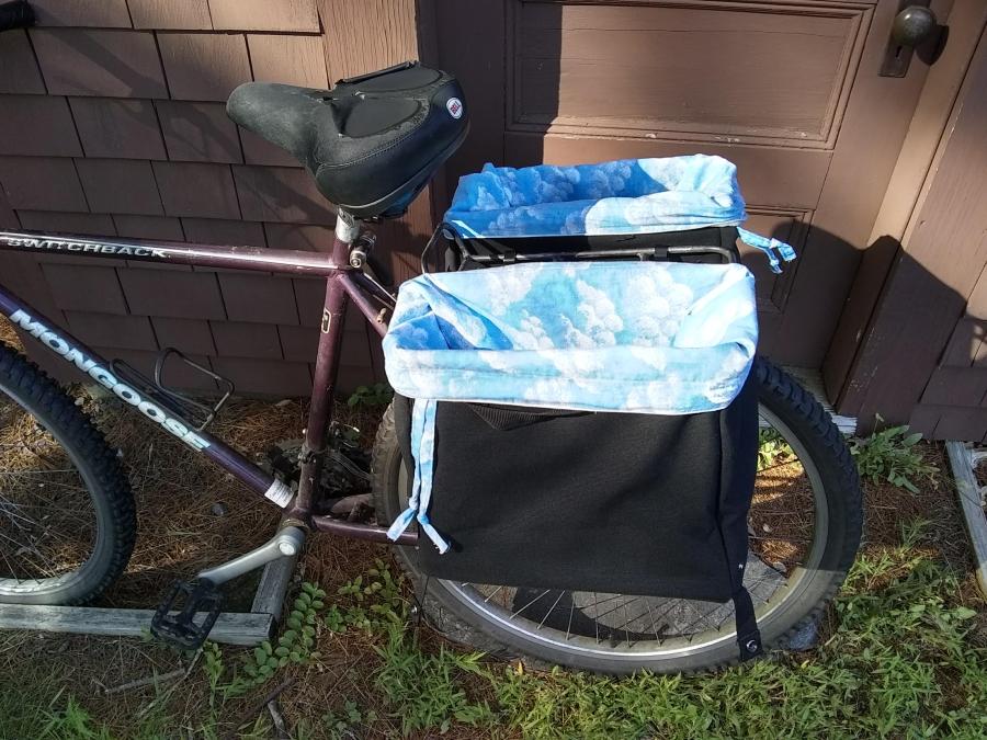 Back side view of bike, with black panniers mounted on rear rack, and blue cloud print bags, open and empty, tucked into panniers