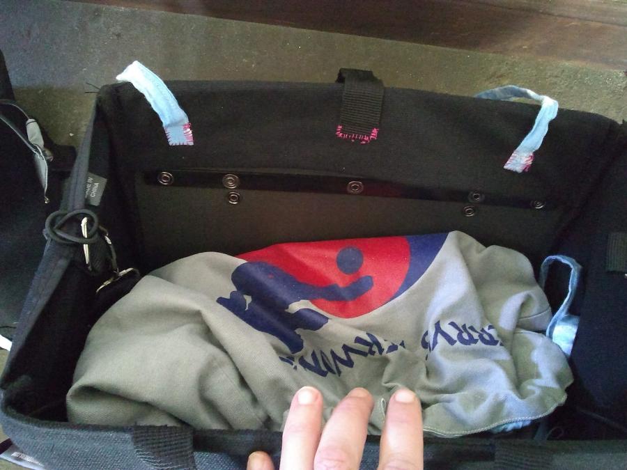 bike pannier, seen from top looking down, with two blue straps on either side of one black strap, all sewn on the inside of the pannier with pink thread. 