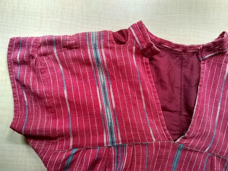 closeup of one side of mended bodice of red woven dress, front view