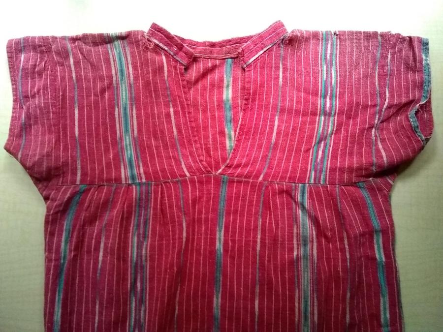 front view of bodice of mostly red woven dress, with holes and frayed fabric visible at shoulders