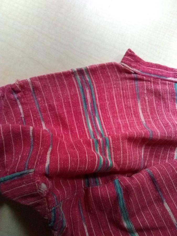 shoulder/armpit area of red woven dress with holes (finger visible through one of the armpit holes)