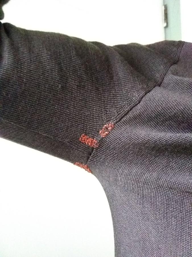 Armpit of brown sweater, worn by person, with small rectangular shaped and persimmon colored darns