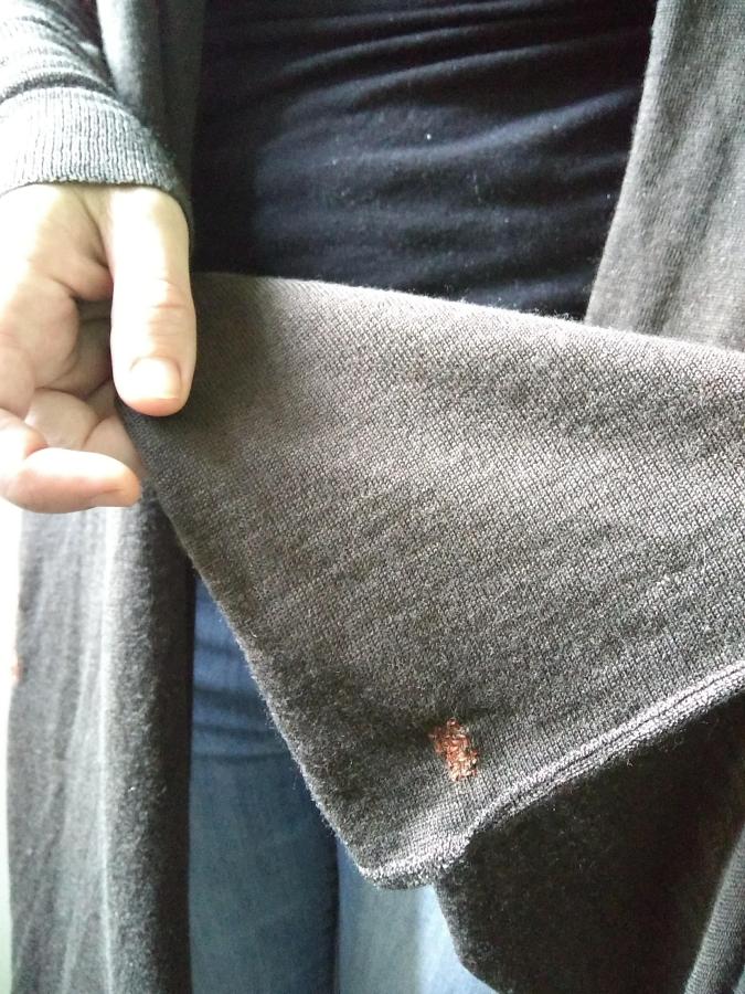 person holding part of the visibly mended (with persimmon thread) brown sweater