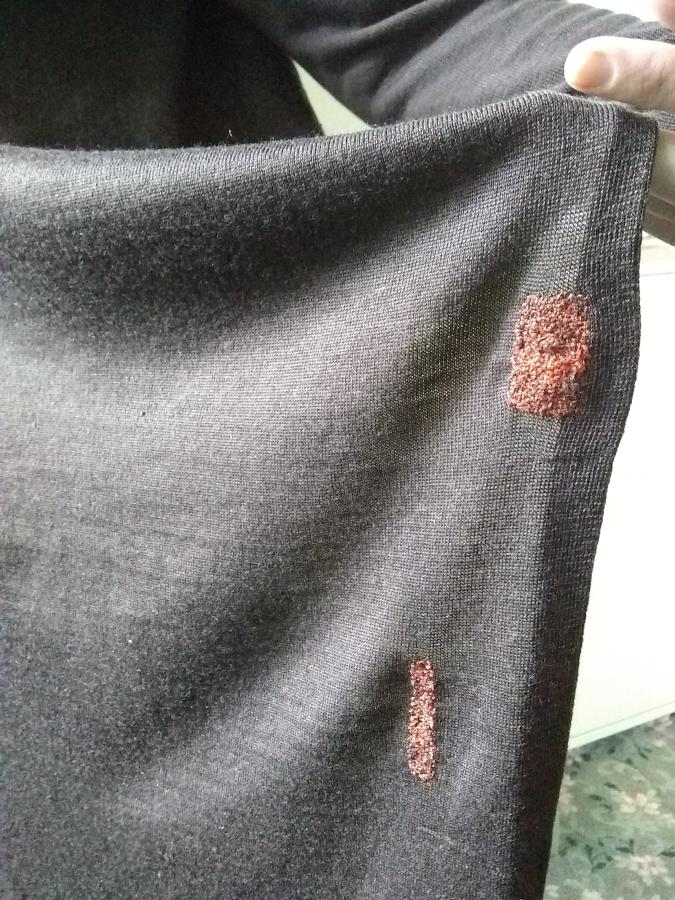 hand holding up sweater with visible darns (persimmon colored, rectangular, on brown sweater)