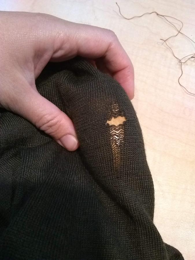 Hand gripping holey sweater with darning egg inside (wood of darning egg visible through the hole)