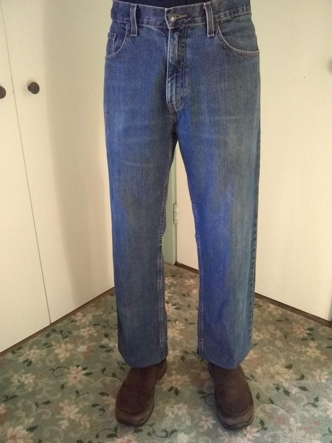 man's legs in blue jeans that are hemmed to fall right above his brown shoes