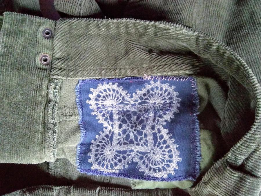 Interior patch on olive corduroy pants: patch is navy fabric with white silkscreen in crochet pattern