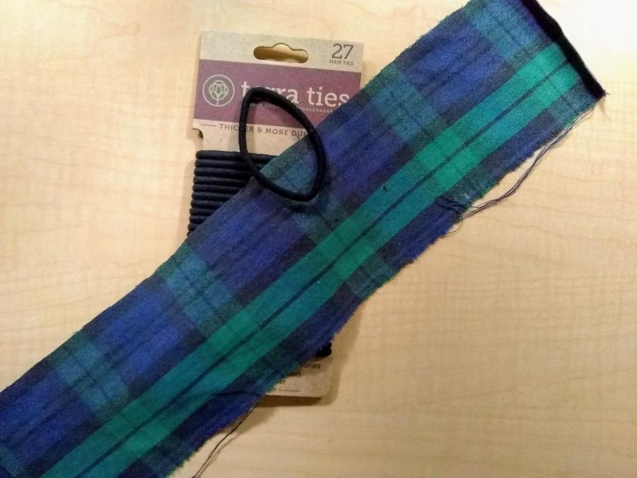 Black watch plaid strip of fabric, round hair elastic, and "terra ties" pack of round elastics on a wooden surface