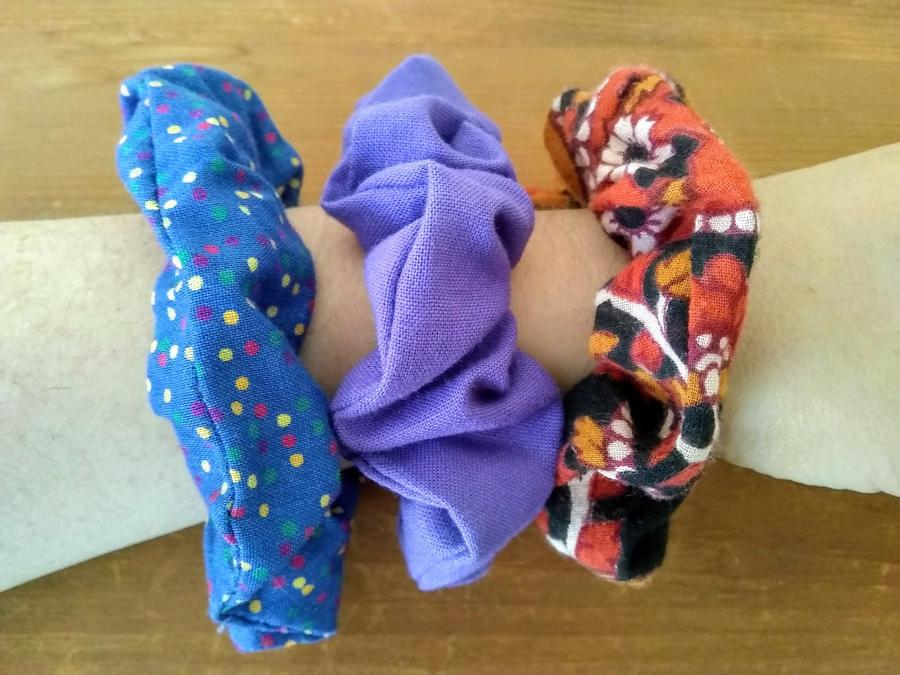 wrist with three scrunchies on it like bracelets: blue with polka dots, purple, and red print