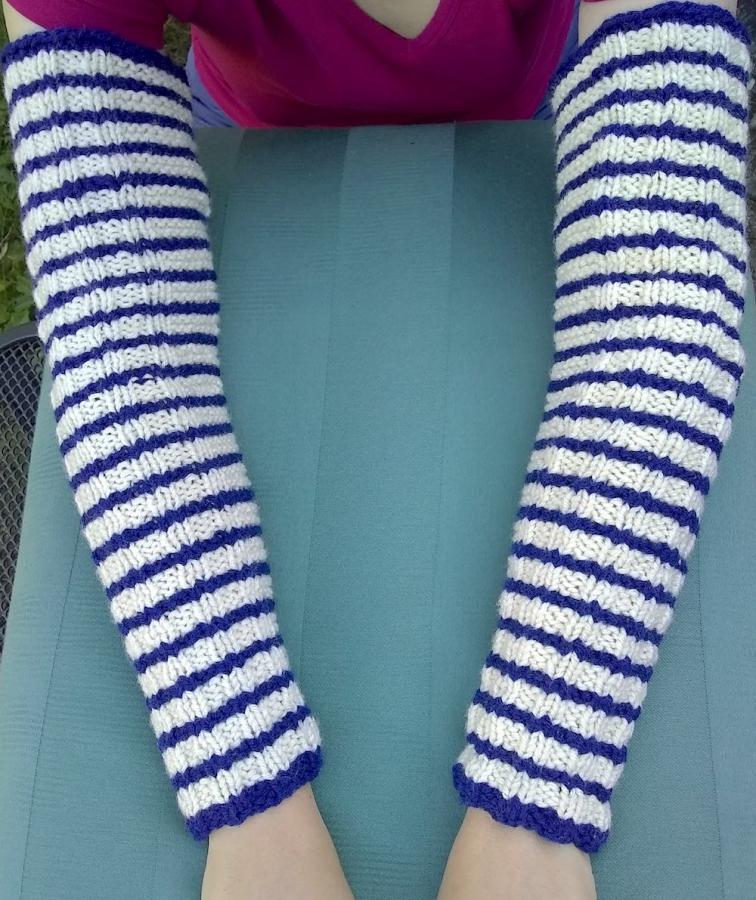 woman with arms outstretched, wearing striped blue and white arm warmers, hand-knit
