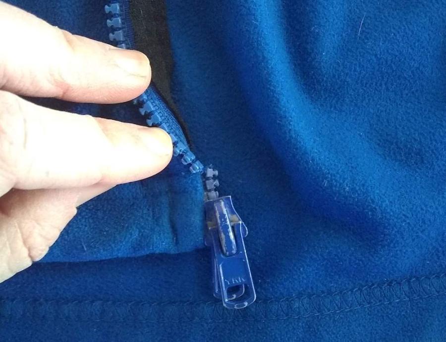 closeup of broken zipper (fingers indicating broken zipper tape) on blue fleece jacket