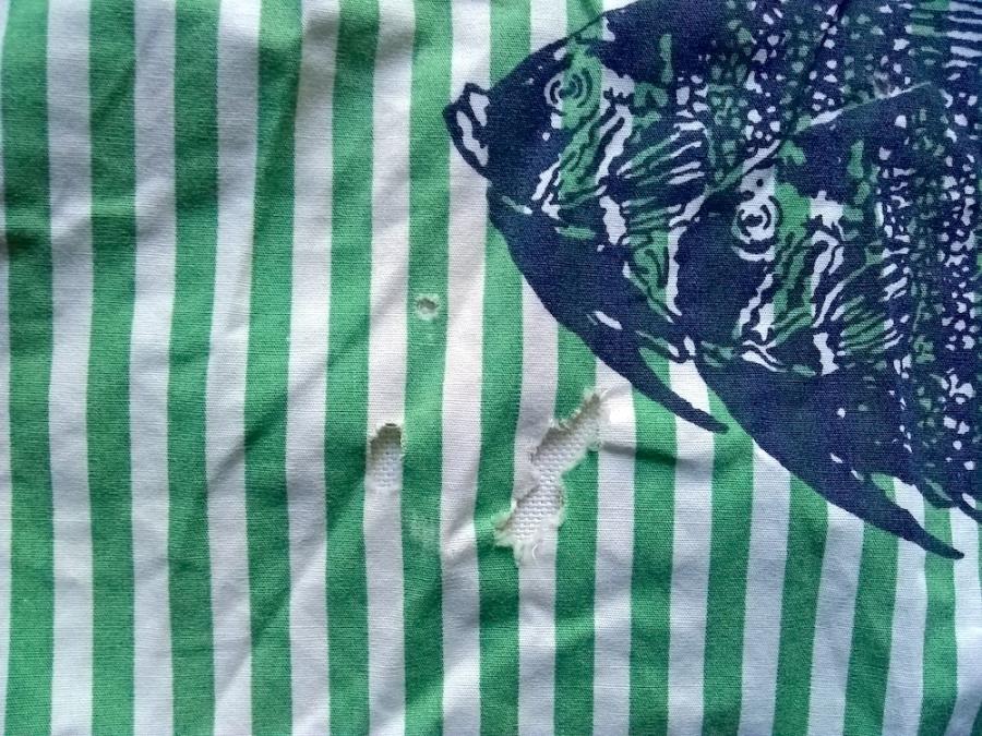 closeup of print fabric, green and white stripes with fish, showing several holes