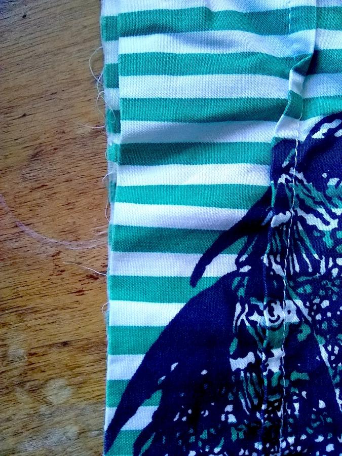 closeup of green and white striped fish print garment, sleeve, showing frayed cuff