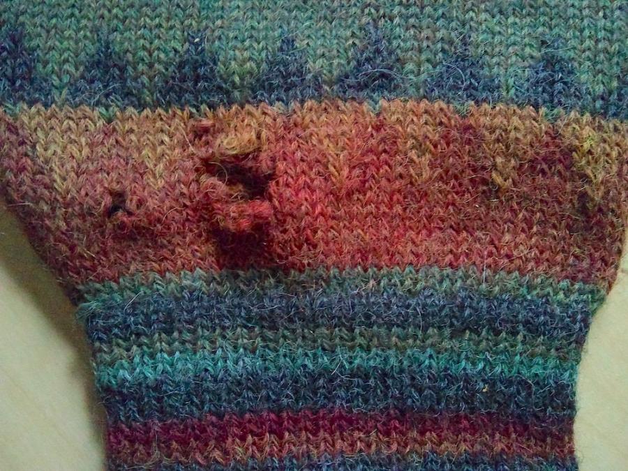 Closeup of wrist of patterned sweater with holes visible